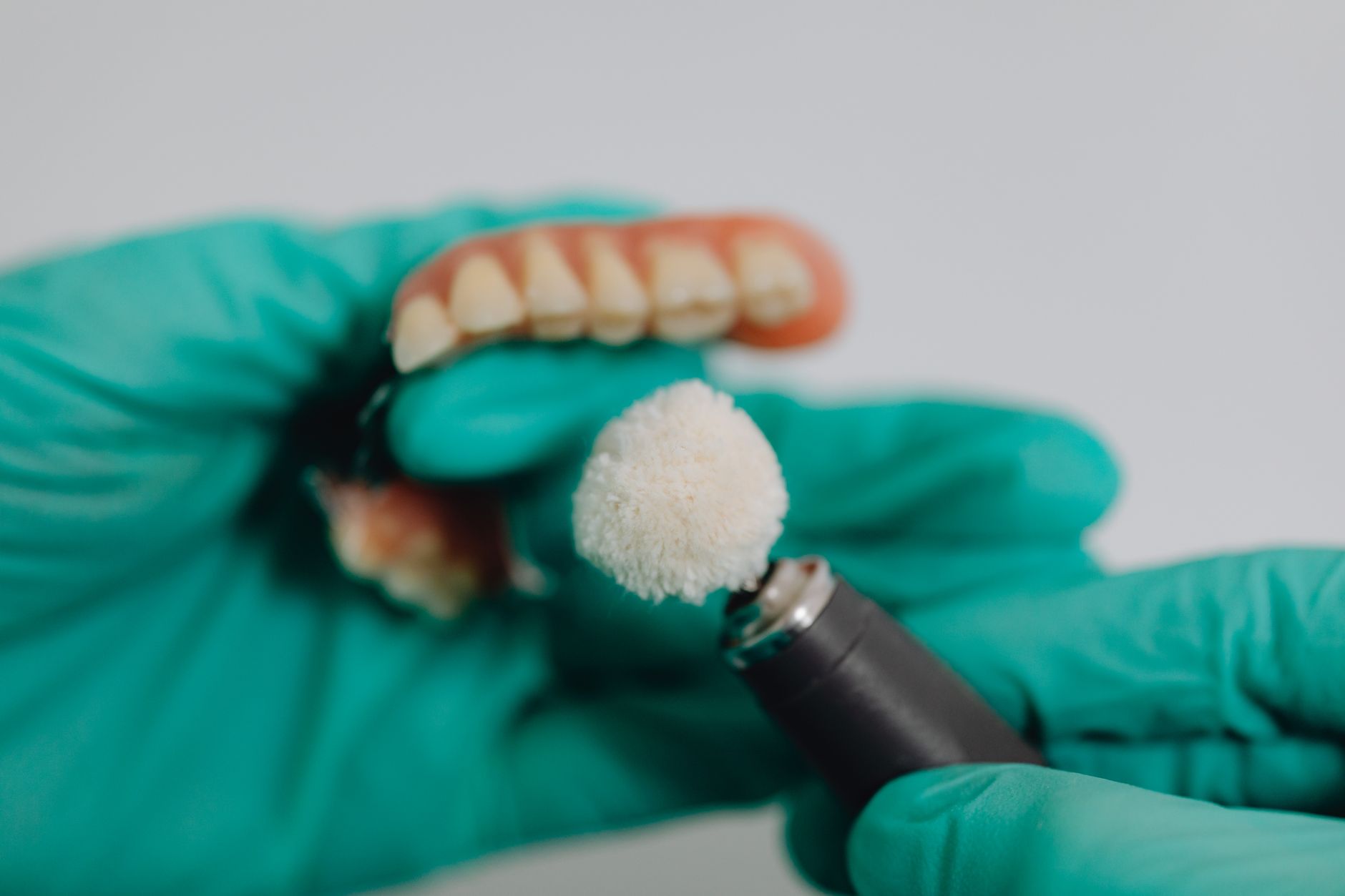 A gloved hand polishing a full denture with a small rotary brush